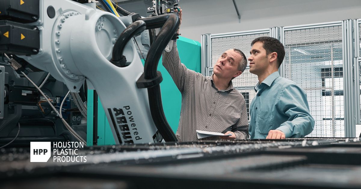 Two engineers examine advanced machinery on a production floor, symbolizing innovation and precision—part of a manufacturing brand refresh for Houston Plastic Products.