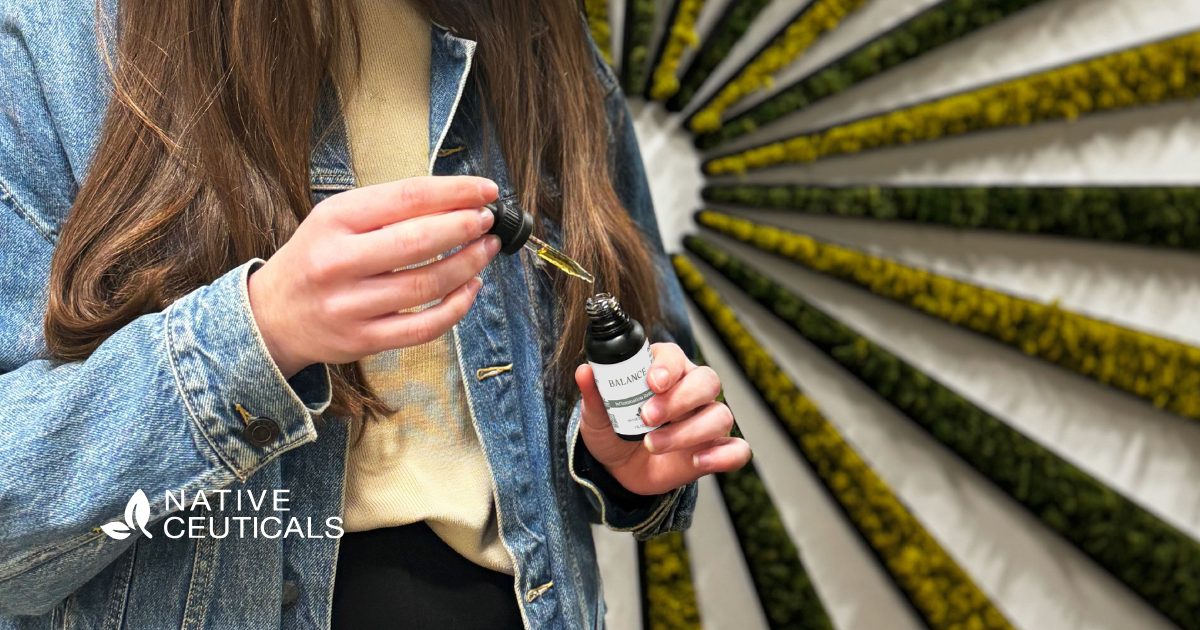 Close-up of a woman using the Native Ceuticals Balance tincture, highlighting the updated packaging design and vibrant brand wall in the background.