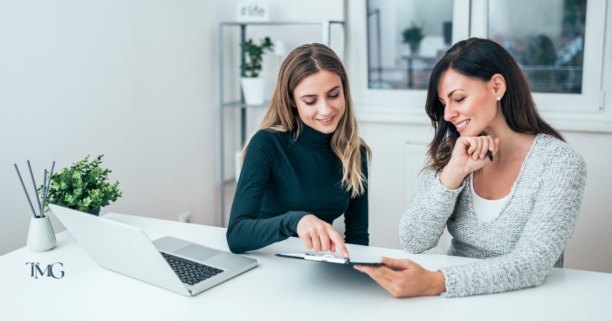 Two women at TMG Marketing Partners collaborating on a brand story strategy with a tablet and laptop in a modern office setting