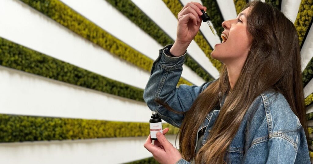 Woman in denim jacket using a Native Ceuticals tincture, showcasing the updated product packaging in a modern wellness setting.