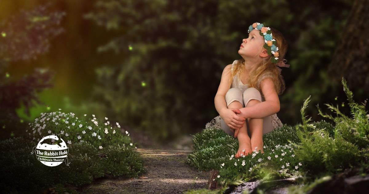 Girl in a flower crown sitting in a magical forest setting with The Rabbit Hole Theater logo, representing storytelling and wonder.