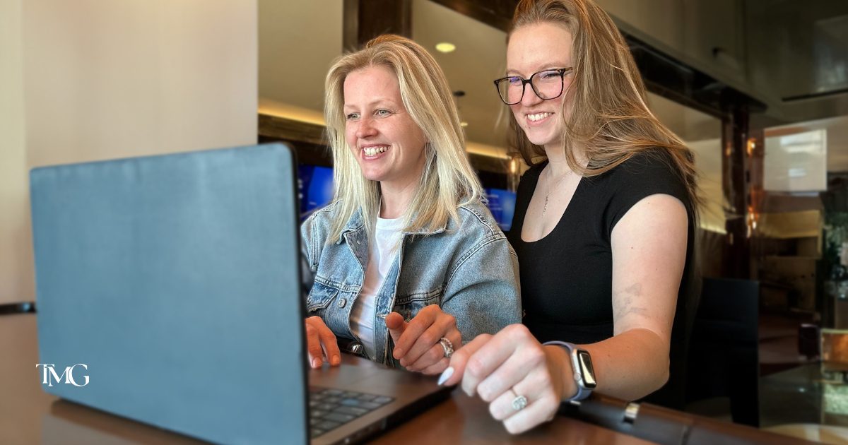 Cristalle, owner of TMG Marketing Partners, and Lilia, Marketing Manager, collaborate on marketing strategy together at a laptop, showcasing teamwork and a streamlined marketing process.