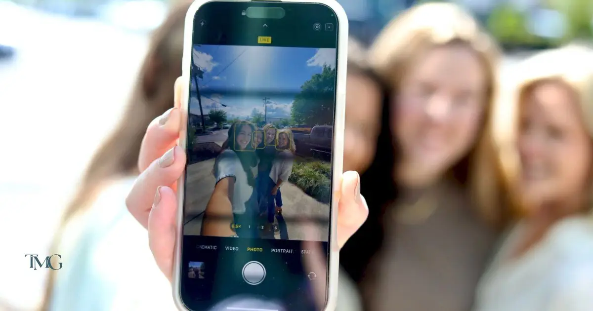 Close-up of a smartphone screen showing four women—Rebecca, Giselle, Lilia, and Cristalle—posing for a selfie outdoors, used to highlight short form content and short form video marketing. The blurred background emphasizes the phone's camera interface, reflecting trends in video marketing for business.