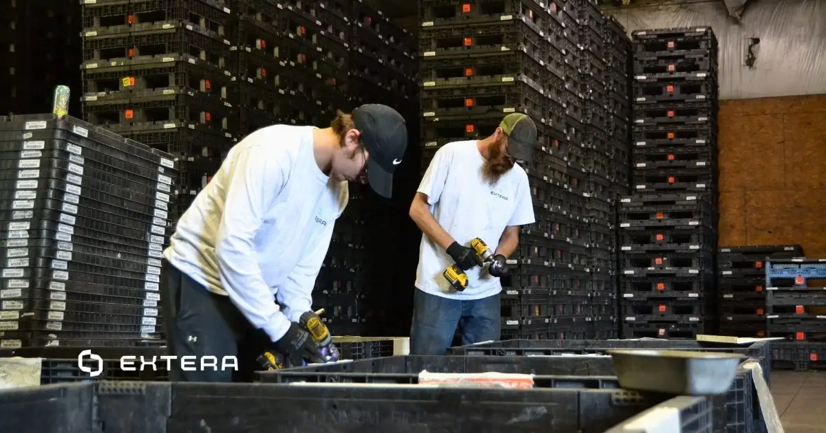 Two workers repairing plastic containers in a warehouse, with tall stacks of black reusable totes in the background. This image supports a case study focused on improving website user experience and responsive web design for a recycling and container company in the plastics industry.