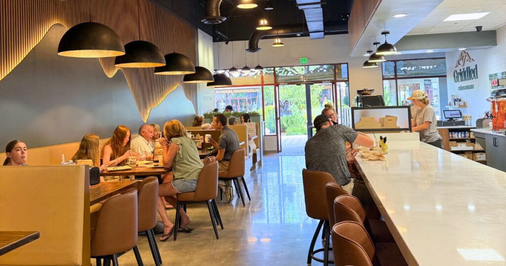 A busy dining room at Griddled Crêpes & Paninis in Castle Rock, CO, with guests seated and staff working the counter.